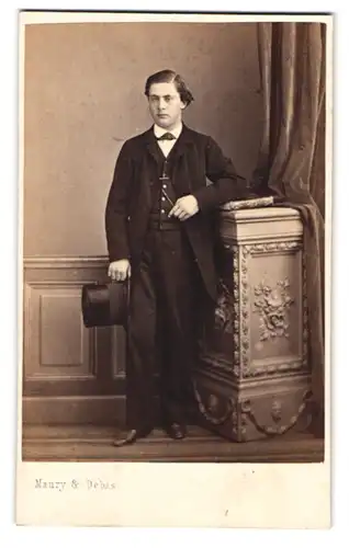 Fotografie Maury & Debas, Paris, Portrait junger Mann im dunklen Anzug mit Zylinder in der Hand