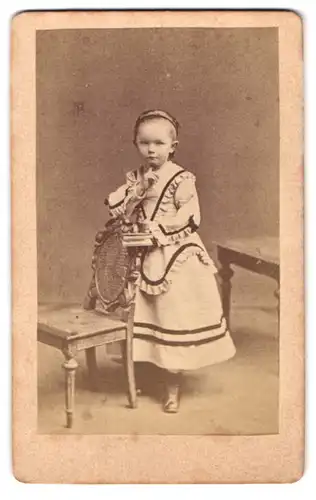 Fotografie unbekannter Fotograf und Ort, Portrait niedliches kleines Mädchen im feinen Kleid stehend am Stuhl