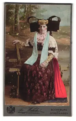 Fotografie Fr. Wehde, Bückeburg, Portrait Dame in Bückeburger Tracht auf einer Holzbank, 1904