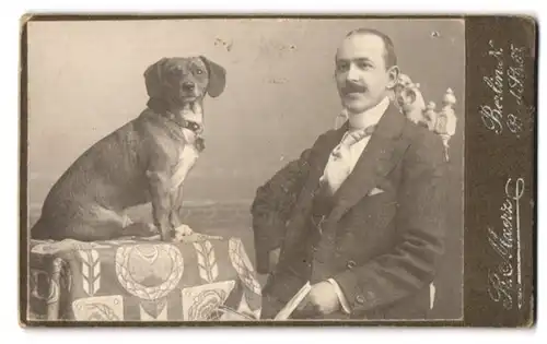 Fotografie R. Maerz, Berlin, Bad-Str. 65, Portrait Herr im Anzug mit Dackemischling auf dem Tisch