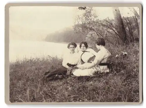 Fotografie unbekannter Fotograf und Ort, drei junge Frauen mit Jugendstil Frisuren sitzen gesellig am See