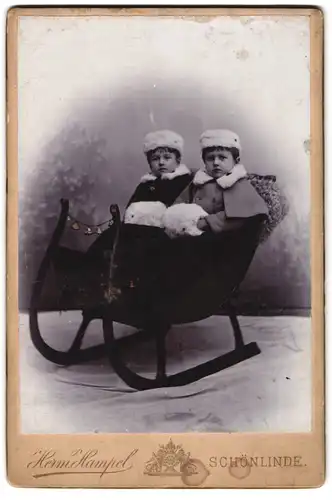 Fotografie Herm. Hampel, Schönlinde, Portrait zwei Kinder in Winterkleidung mit Muff in einem Schlitten