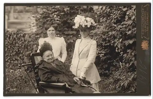 Fotografie H. Schlitzberger, Bad Pyrmont, Portrait drei Damen in Biedermeierkleidern mit Rollstuhl