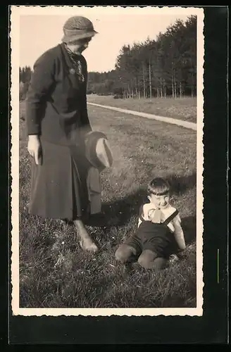 Foto-AK Kleiner Junge mit Topfschnitt spielt zum Ärger seiner Mutter im Gras