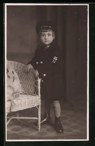 Foto-AK Kleinkind in Uniform der Marine posiert neben einem Korbstuhl