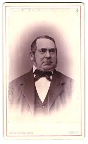 Fotografie Herm. Linde, Lübeck, Portrait korpulenter Herr im Anzug mit Kinnbart und Fliege