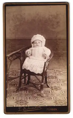 Fotografie L. Schradler, Füssen, Portrait Kleinkind fest eingepackt im Wollkleid mit Mütze