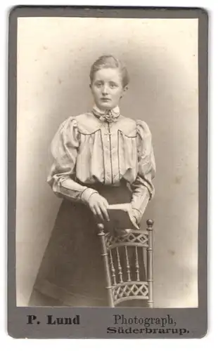 Fotografie P. Lund, Süderbrarup, Portrait hübsches junges Mädchen in seidener Bluse mit Schleife am Stuhl stehend