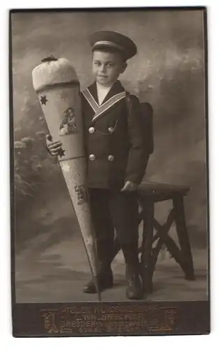 Fotografie L. Walbecker, Dresden, Portrait junger Knabe in Schuluniform mot grosser Zuckertüte und Schulranzen