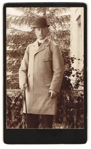 Fotografie unbekannter Fotograf und Ort, Portrait Herr im Anzug mit Melone und Flanierstock trägt Mantel