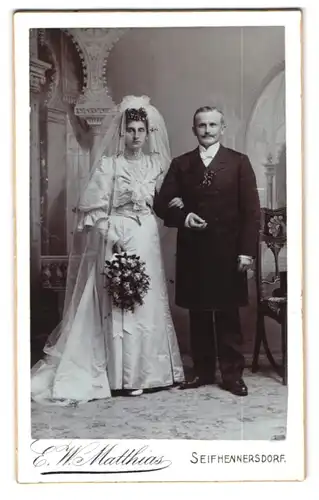 Fotografie E. W. Matthais, Seifhennersdorf, Brautleute im Hochzeitskleid und Anzug, Brautstrauss