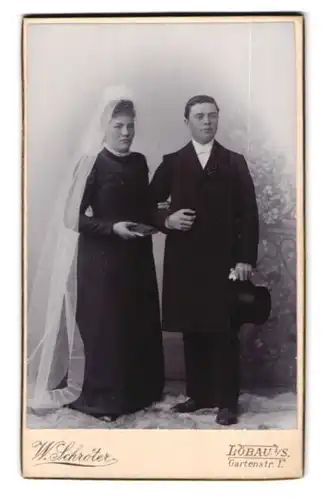 Fotografie W. Schröter, Löbau i. S., Gartenstr. 1, Brautleute im schwarzen Hochzeitskleid und Anzug mit Zylinder