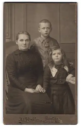 Fotografie Ad. Winkler, Görlitz, Portrait Mutter im dunklen Kleid mit ihren beiden Kindern im Atelier, Mutterglück