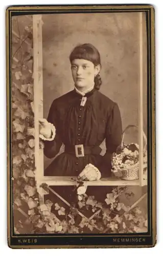 Fotografie H. Weis, Memmingen, junge Frau im schwarzen Kleid stehend am Fenster mit einem Blumenkorb