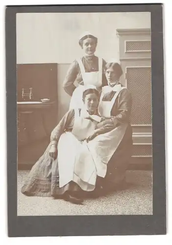 Fotografie unbekannter Fotograf und Ort, drei Dienstmädchen in Uniform mit Schürzen posieren im Atelier