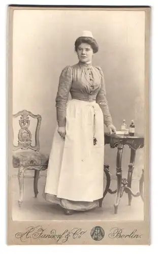 Fotografie A. Jandorf & Co., Berlin, Gr. Frankfurterstr. 113, junge Krankenschwester in Uniform mit Medizinflaschen