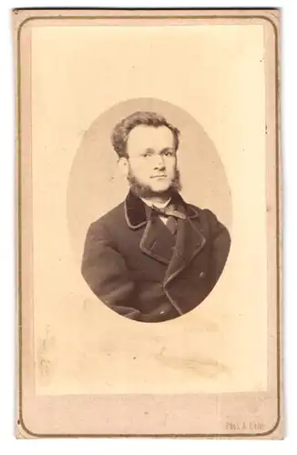 Fotografie Amand Helm, Prag, Mariengasse 919, junger Mann mit Backenbart und Brille im Mantel