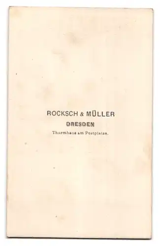 Fotografie Rocksch & Müller, Dresden, a, Postplatz, Portrait Mann im dunklen Anzug mit Fliege vor einer Studiokulisse