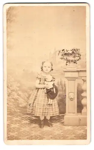 Fotografie C. Grust, Meissen, Rothe Stufen 29, niedliches kleines Mädchen im karierten Kleid mit ihrer Puppe im Arm