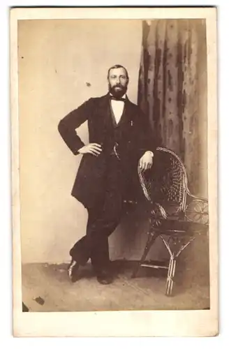 Fotografie unbekannter Fotograf und Ort, Portrait junger Mann im schwarzen Anzug mit Vollbart lehnt an einem Stuhl
