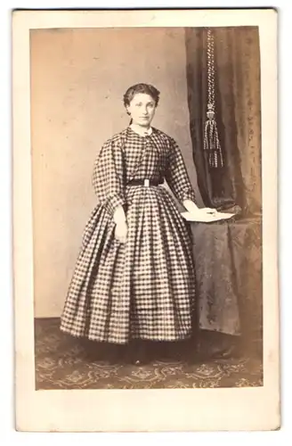 Fotografie P. B. Jensen, Hamburg, Steinstr. 82, Portrait junge Dame im karierten Kleid am Tisch stehend