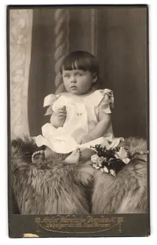 Fotografie Bruno Wendsche, Dresden-N., Leipzigerstr. 58, Süsses Kleinkind im weissen Kleid sitzt auf Fell