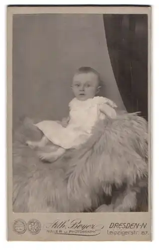 Fotografie Arth. Beyer, Dresden-N., Leipzigerstr. 87, Süsses Kleinkind im Weissen Kleid sitzt auf Fell