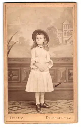 Fotografie Eulenstein, Leipzig, süsses kleines Mädchen im weissne Kleid mit Locken und Sommerhut, Studiokulisse