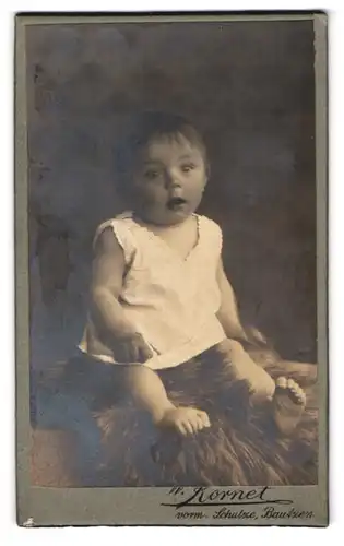 Fotografie W. Kornet, Bautzen, Süsses Kleinkind im Hemd sitzt auf Fell