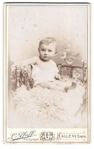 Fotografie L. Pfaff, Halle a. d. Saale, Geiststr. 47, Süsses Kleinkind im Hemd sitzt auf Fell
