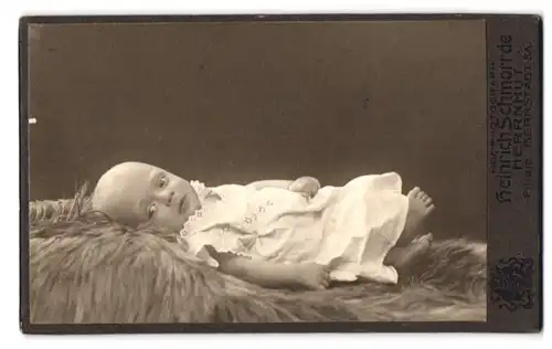 Fotografie Heinrich Schmorrde, Herrnhut, Bernstadt /Sa., Süsses Kleinkind im Kleid liegt auf Fell