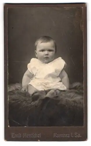 Fotografie Ernst Hentschel, Kamenz i. Sa., Hoyerswerdaerstr. 30, Portrait niedliches Baby auf einem Fell sitzend