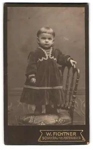 Fotografie W. Fichtner, Schandau a. E., Poststr. 31, Portrait süsses kleines Mädchen im Samtkleid auf einem Stuhl stehend