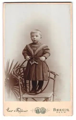 Fotografie Max Steffens, Berlin, Lothringer Str. 54, Kleinkind mit Spielreifen steht auf Stuhl