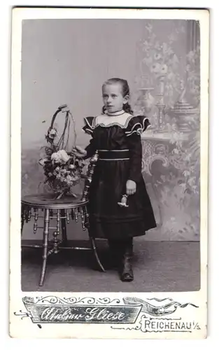 Fotografie Atelier Gliese, Reichenau i/S., Kleines Mädchen in Kleid steht neben blumenarrangement