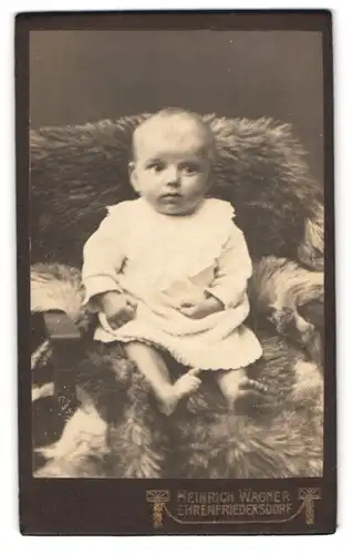 Fotografie Heinrich Wagner, Ehrenfriedersdorf, Kleinkind in weissem Kleid sitzt auf mit Fell gepolsterten Stuhl