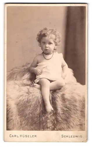 Fotografie Carl Hüseler, Schleswig, Stadtweg 34, Portrait sés blondes Mädchen mit lockigem Haar auf Fell sitzend