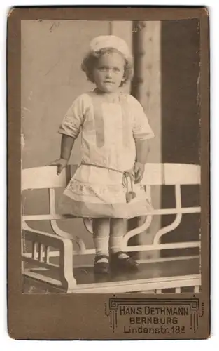 Fotografie Hans Dethmann, Bernburg, Lindenstr. 18a, Portrait blondes süsses Mädchen mit Mütze im bestickten Kleidchen