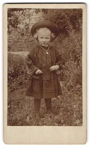 Fotografie unbekannter Fotograf und Ort, Portrait niedliches blondes Mädchen steht in Kleid & Hut im Garten