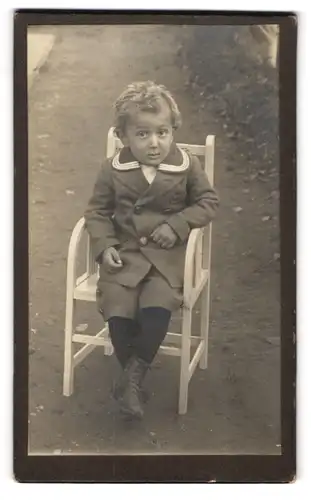 Fotografie unbekannter Fotograf und Ort, frecher Bube sitzt im Matrosenanzug auf einem Gartenstuhl