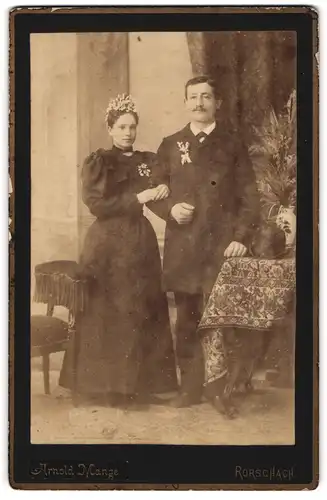 Fotografie Arnold Mange, Rorschach, Portrait junges Brautpaar im schwarzen Kleid und Anzug nebst Melone