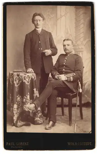 Fotografie Paul Lorenz, Wolmirstedt, Sitzender Solat in Uniform mit Säbel und Herr mit gelocktem Haar