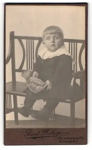 Fotografie Paul Bethge, Fürstenberg a. O., Wilhelmstr. 1, Kleinkind im Kleid mit seinem Teddy auf einer Bank sitzend