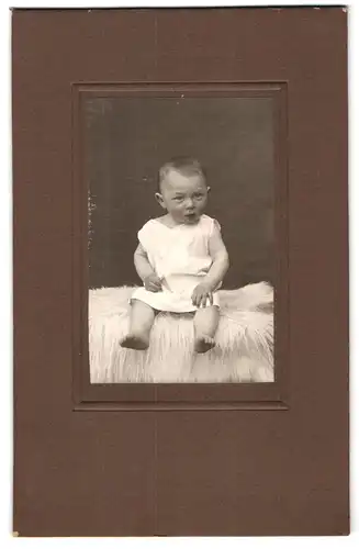 Fotografie unbekannter Fotograf und Ort, Süsses Kleinkind im Hemd sitzt auf Fell