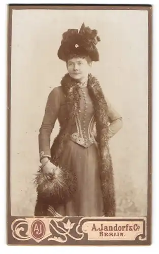 Fotografie A. Jandorf & Co., Berlin, Portrait junge Dame im taillierten Kleid mit Federboa, Muff und Hut