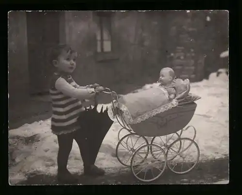 Fotografie Spielzeug, Knabe schiebt Puppenwagen mit Puppe durch den Schnee