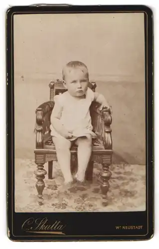 Fotografie Carl Skutta, Wr. Neustadt, Bahngasse 27, Kleinkind in kuzem Kleidchen auf einem Sessel