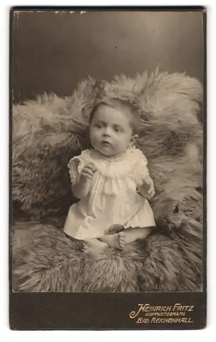 Fotografie Heinrich Fritz, Bad-Reichenhall, Süsses Kleinkind im Hemd sitzt auf Fell