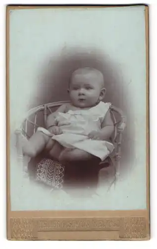Fotografie Gustav Simon, Melk a. d. D., Halbnacktes Kleinkind im Hemd sitzt im Korbstuhl