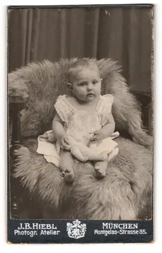 Fotografie J. B. Hiebl, München, Montgelasstrasse 35, Süsses Kleinkind im Kleid sitzt auf Fell